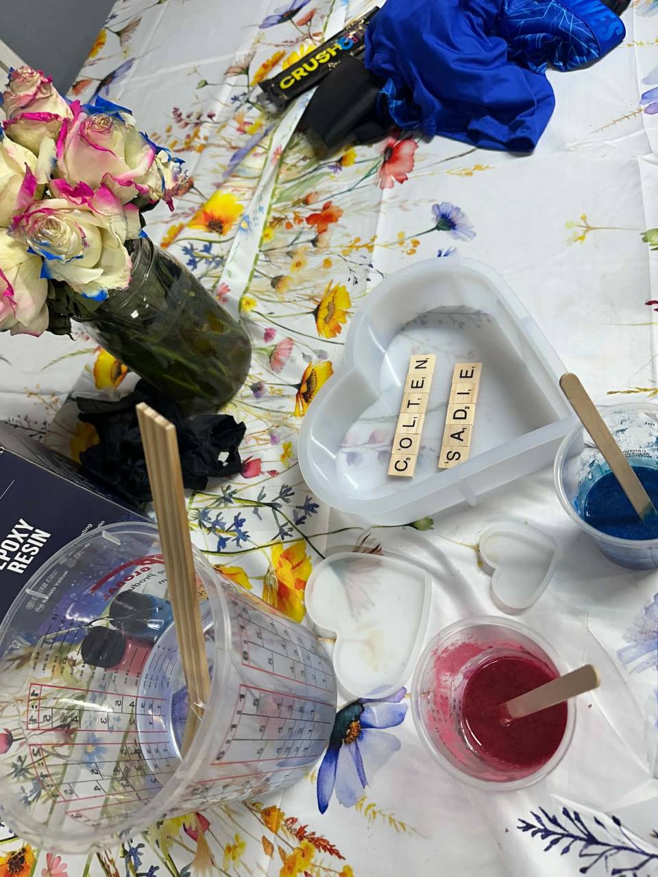 A pour in progress: cups of blue and pink pigment, letter tiles, and a heart mold on the table